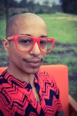 image of ignacio who is bald wearing orange glasses, sitting on an orange chair, with an orange tunic with black zig-zag stripes