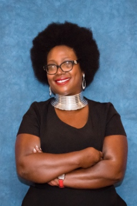 photo of DonYeta. she is a black woman with an afro, large silver necklace, and her arms are crossed.